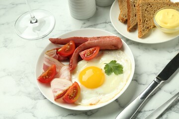 Tasty brunch. Fried egg, sausage, bacon and tomatoes on white marble table, closeup