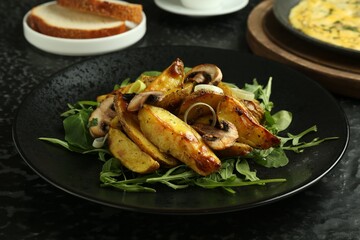 Tasty brunch. Delicious fried potatoes with arugula and mushrooms served on black textured table, closeup