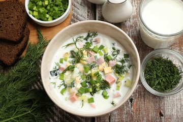 Delicious okroshka soup in bowl on wooden table, flat lay