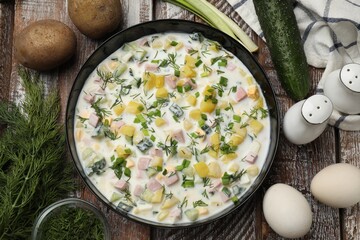 Delicious okroshka soup with kefir in bowl and ingredients on wooden table, flat lay
