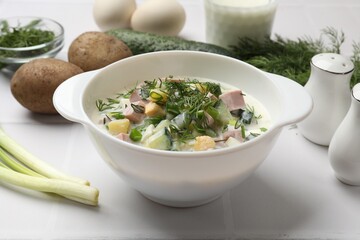 Delicious okroshka soup in bowl and ingredients on white table, closeup