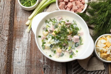 Delicious okroshka soup in bowl and ingredients on wooden table, flat lay. Space for text