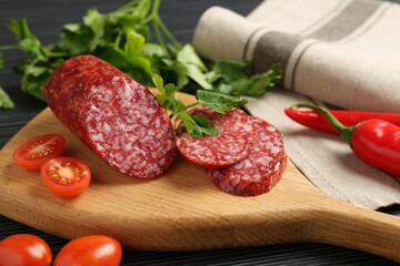 Cut smoked sausage, parsley and tomatoes on black wooden table, closeup