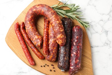 Different smoked sausages, rosemary and peppercorns on white marble table, top view