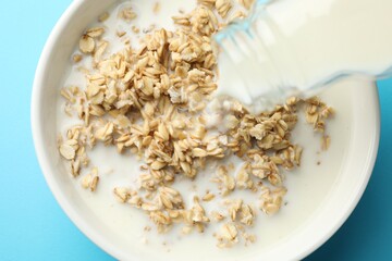 Pouring milk into bowl with oatmeal at light blue table, top view