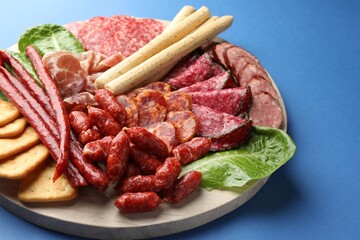 Different smoked sausages and other snacks on blue background, closeup