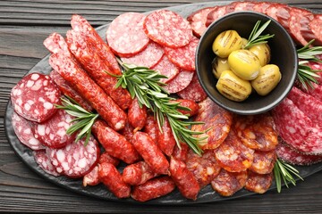 Different smoked sausages, olives and rosemary on wooden table, top view