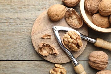 Fresh walnuts and nutcracker on wooden table, flat lay. Space for text