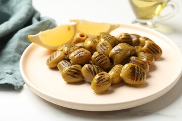 Grilled green olives and lemon wedges on light table, closeup