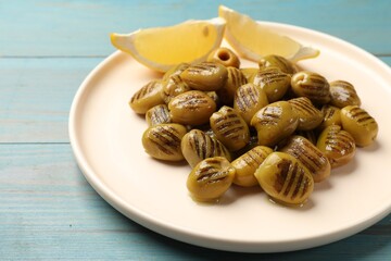 Grilled green olives and lemon wedges on light blue wooden table, closeup