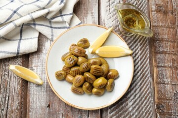 Grilled green olives, lemon wedges and oil on wooden table, flat lay