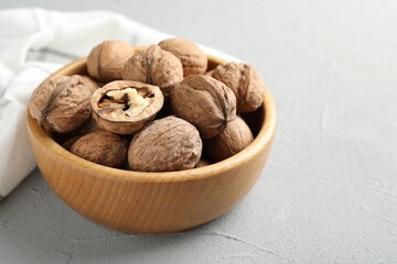 Fresh walnuts in bowl on gray table, closeup. Space for text