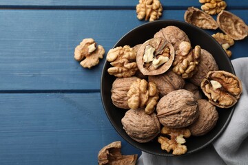 Fresh walnuts in bowl on blue wooden table, flat lay. Space for text