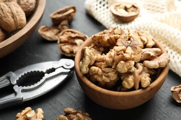 Fresh ripe walnuts in bowl and nutcracker on black table, closeup