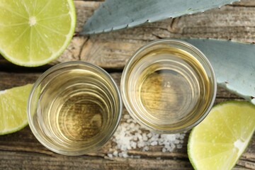 Mexican tequila shots, slices of lime, salt and agave leaves on wooden table, flat lay
