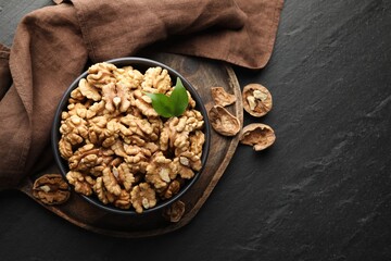 Fresh ripe walnuts in bowl and shells on black table, top view. Space for text
