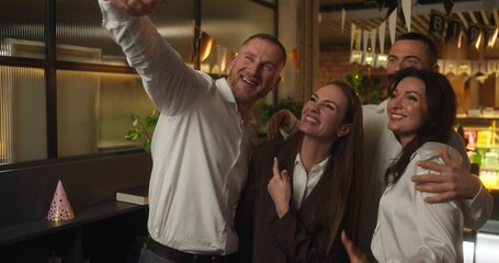 Four happy office workers in business clothes take a selfie and rejoice during a fun corporate party