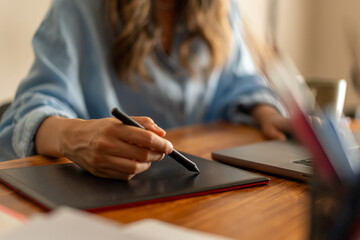 Graphic designer using digital tablet and stylus for creative work at desk