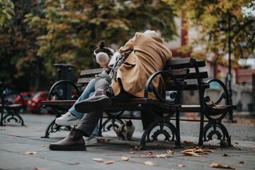 A loving couple sits closely on a park bench, surrounded by falling autumn leaves. They enjoy a...