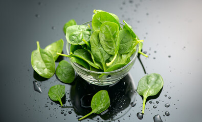 Spinach in a transparent glass bowl on gray background with reflection. Heap of Baby spinach fresh leaves close up, water drops, Healthy vegan food, diet, dieting, vitamin concept 