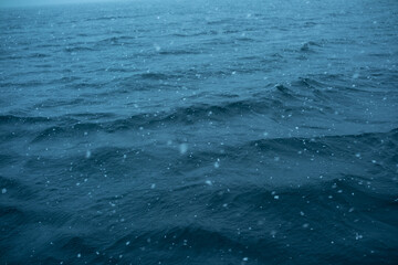 Waves ripple under falling snow on a quiet ocean in winter