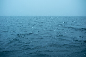 Calm sea with gentle waves and falling snow during winter season