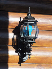 Decorative outdoor lantern is mounted on wooden wall with blue bulb.
