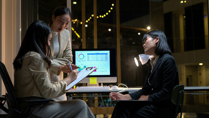Fototapeta premium Three women are sitting at a desk with a computer monitor in front of them
