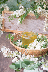 still life of a full jar of transparent yellow ocacia honey on the table against the background of wax honeycombs, organic enriched beekeeping product for alternative medicine,