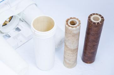 Dirty used set of filter cartridges of a three-stage water filter with a coating of metal impurities on a white background