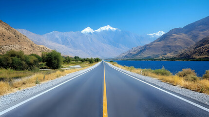 Fototapeta premium Open Road Leads to Majestic Snow-Capped Mountains and Serene Lake Under Blue Sky