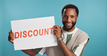 Portrait, discount board and black man with smile, opportunity and promotion on blue studio background. African person, model and guy with options, billboard and poster with banner and announcement