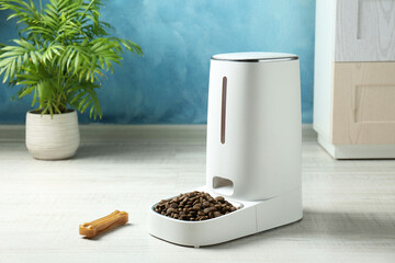 Dry pet food in automatic feeder and chew bone on floor indoors