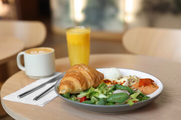 Tasty breakfast. Freshly baked croissant and salad served on wooden table in cafe, closeup