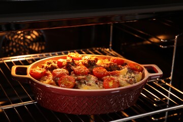 Delicious pasta casserole with cheese, tomatoes and minced meat in baking dish in oven, closeup