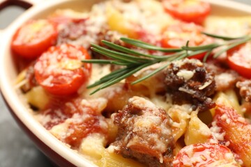 Delicious pasta casserole with cheese, tomatoes, minced meat and rosemary in baking dish, closeup