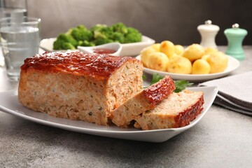 Delicious baked turkey meatloaf with vegetables served on grey table, closeup