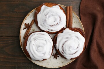Tasty cinnamon rolls with cream and spices on wooden table, top view