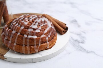 Tasty cinnamon roll with cream on white marble table, closeup. Space for text