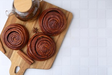 Delicious cinnamon rolls, tea and spices on white tiled table, top view. Space for text
