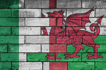 Obraz premium colourful painted big flag of italy and flag of wales on a massive old brick wall background. concept