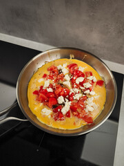 Cooking cheesy omelette with ripe tomatoes in skillet, romantic morning meal for couples