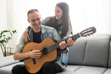 smiling father showing daughter how to play barre chord
