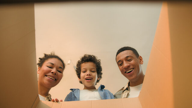 Point of view POV open box African american family parents son unpacking cardboard parcel happy funny little boy child kid surprise teddy bear toy birthday present moving day online shopping delivery