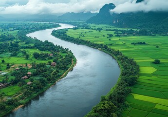Fototapeta premium River winds through the hills of Bandarban, Bangladesh, embraced by misty clouds and lush greenery. Mountains loom under overcast skies above a dense rural forest