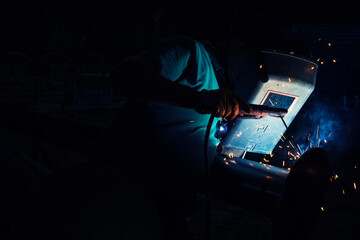 Worker use weld metal welding machine in workshop, blue sparks.