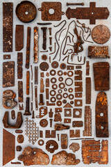 A group of various old rusty parts arranged on a concrete surface. Old rusty nuts, bolts, nails and other parts flay lay on gray background.