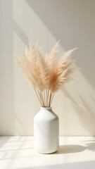 A white ceramic vase holds delicate dried pampas grass against a soft background, illuminated by gentle sunlight, creating a serene and minimalistic atmosphere