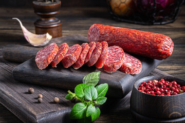Sliced salami on dark wooden board with spices and herbs