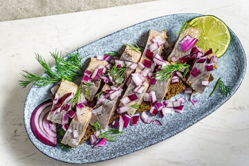 Herring fillets on rye bread, garnished with red onion, dill and lemon